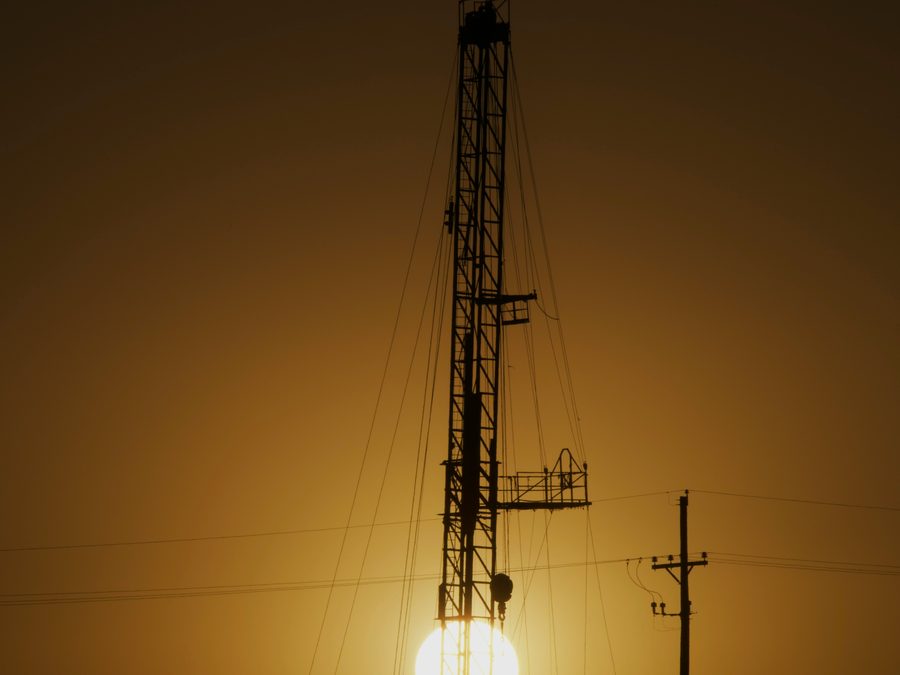 Drilling rig and pumpjacks silhouetted against a golden sunset with power lines running to the lease in South Texas